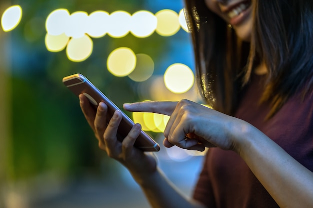 Foto close-uphand van aziatische vrouw gebruikend smartphone en wat betreft het scherm bij openluchtpark