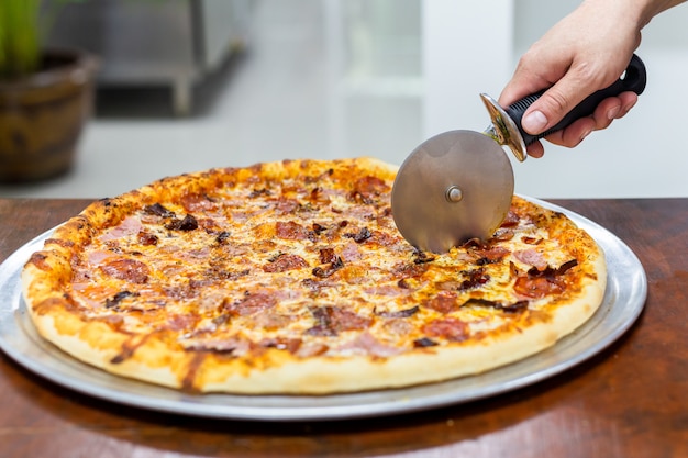 Close-uphand van chef-kok scherpe pizza op lijst.