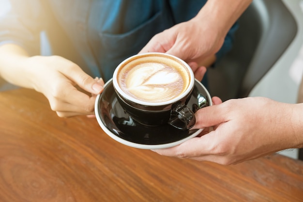 Close-uphand van een serveerster die een kop van koffie dienen aan klant.