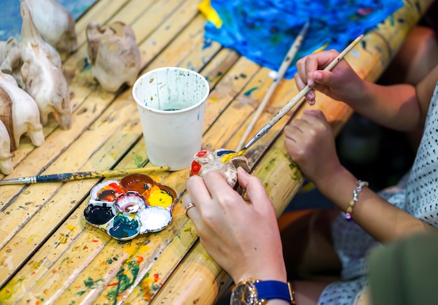 Close-uphanden van kunststudenten die verfborstelstudie houden en verf op houten dierlijke pop in het kunstklaslokaal leren.