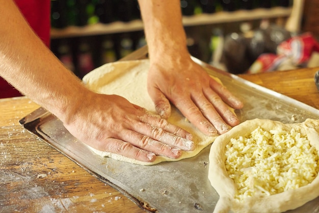 Close-uphanden van mannelijke bakker die traditionele Georgische keukenchachapuri voorbereiden