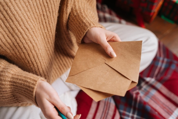 Close-uphanden van onherkenbare jonge vrouw die lege envelop en pen houden die het schrijven van brief voorbereiden