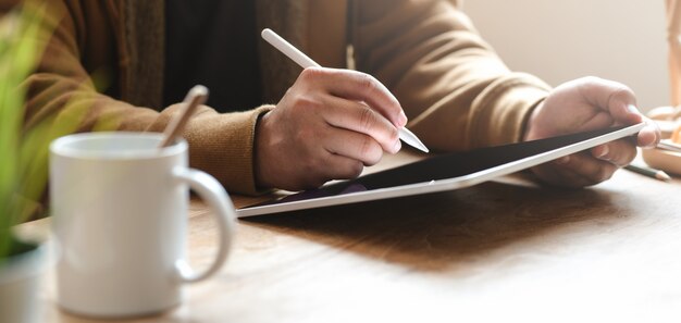 Close-upmening van de mens die aan zijn project werken terwijl het gebruiken van tablet in zijn comfortabel bureau