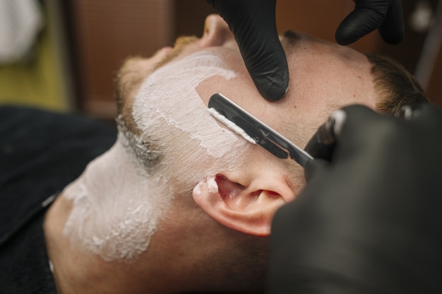 Close-upmening van de mens die zijn baard scheert bij herenkapper