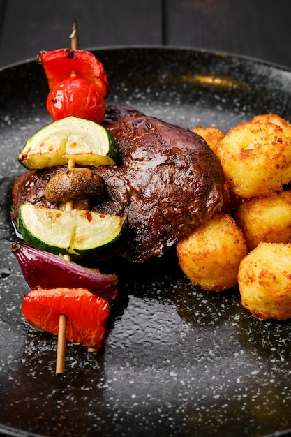 Close-upmening van geroosterd rundvlees met groenten en aardappelballen op een plaat