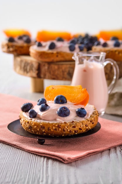 Close-upmening van zoete broodjes met yoghurt, bosbes en plak van dadelpruim op witte houten lijst