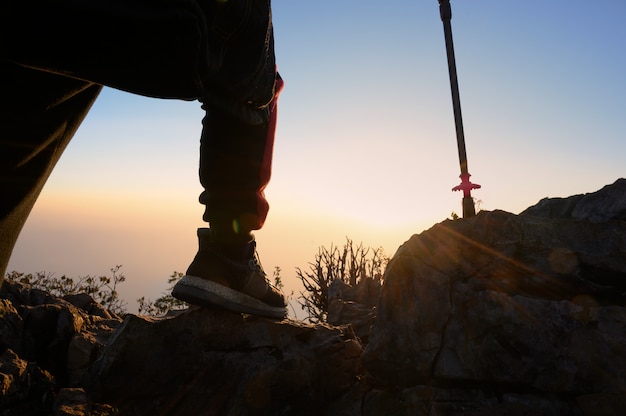 Close-upmens die bij de berg van het zonsondergangsilhouet wandelen met het avontuurconcept van de reislevensstijl