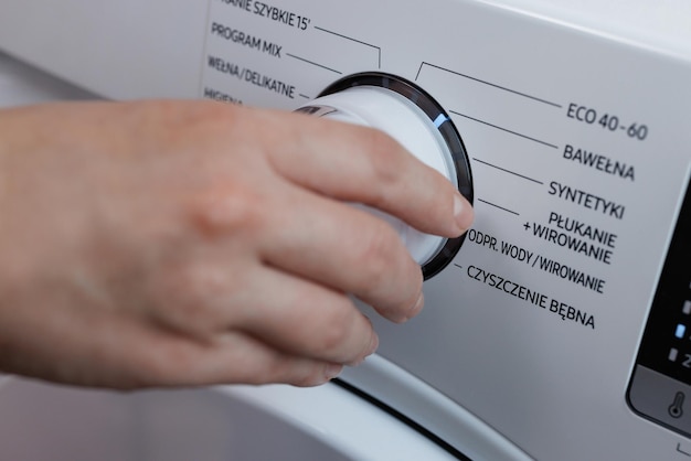 Close-upopnamen waarbij een hand aan de knop op het voorpaneel draait en de wasmachine uitschakelt