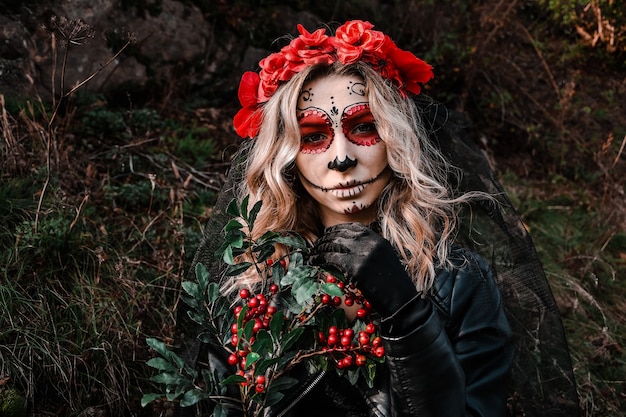 Close-upportret van calavera catrina. jonge vrouw met de make-up van de suikerschedel en rode bloemen. dia de los muertos. dag van de doden. halloween. santa muerte make-up vrouw op halloween vooravond. mode creatief