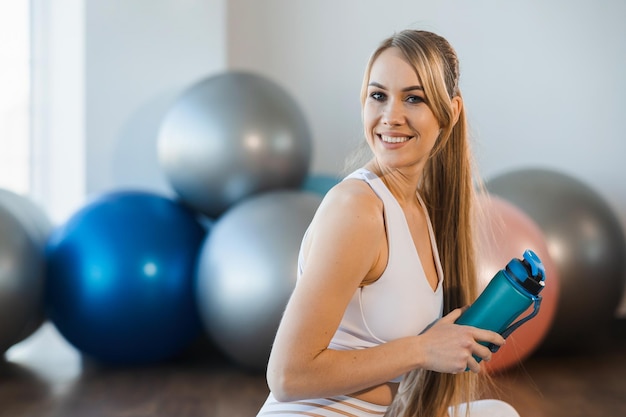 Close-upportret van een glimlachende vrouw met een bidon in de fitnessstudio