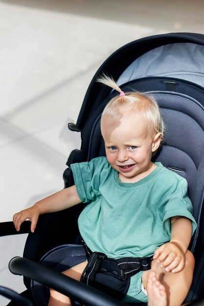 Close-upportret van een klein kind in een vervoermamma met blondebabymeisje die in groene kleren a lopen