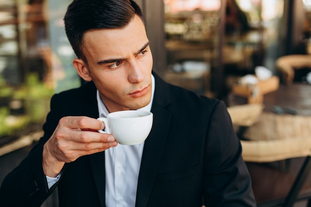 Close-upportret van een kop van koffie houden en zakenman die zijdelings kijken - Beeld