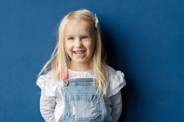 Close-upportret van gelukkig blondejarenmeisje tegen blauwe muur