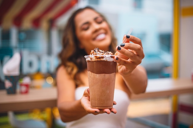 Close-upportret van gelukkige aantrekkelijke glimlachende vrouw die een chocolademilkshake houdt met nadruk op milkshake