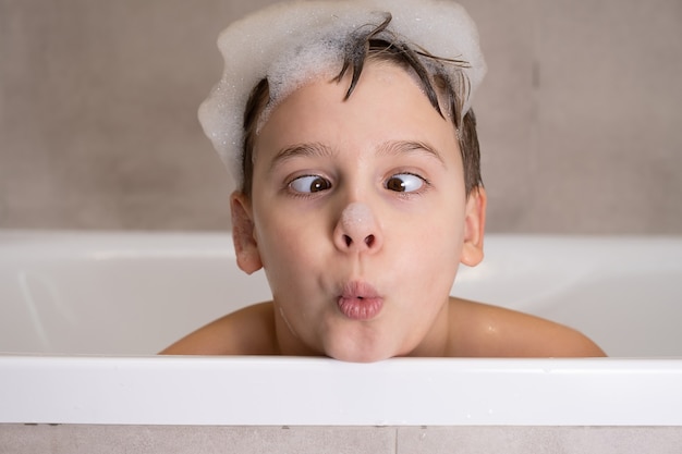 Close-upportret van grappige jongen die met water en schuim in badkamers speelt Leuk gelukkig kind baadt en maakt grappige gezichten gezonde kinderjaren