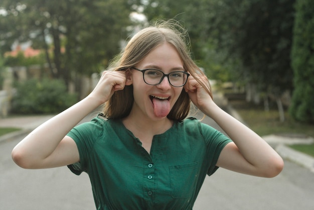 Foto close-upportret van het grappige tienermeisje glimlachen, hebbend pret in groene kleding en open mond met geplakte tounge.