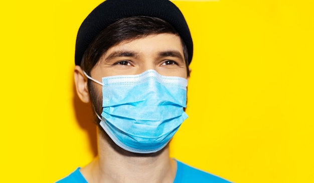 close-upportret van jonge kerel die medisch gezichtsmasker draagt tegen coronavirus op gele kleur
