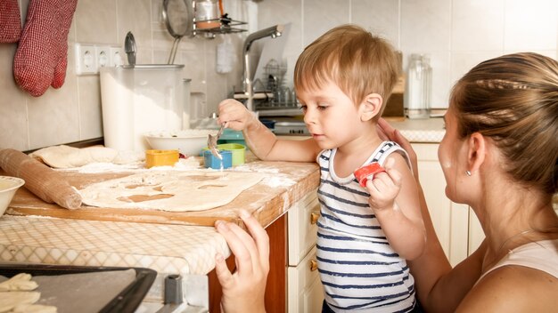 Close-upportret van jonge moeder met peuterjongen die bakpan houdt en koekjes op keuken maakt