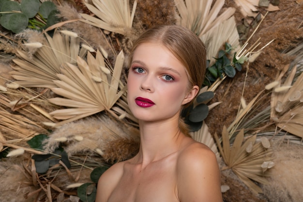 Close-upportret van jonge mooie vrouw met een gezonde huid van het gezicht. blond meisje met bourgondische lippen tegen een achtergrond van lente droge veld bloemen. schoonheid gezichtsverzorging concept.