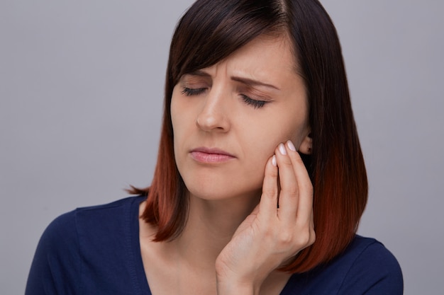 Close-upportret van jonge vrouw die aan sterke hoofdpijn lijden, vingers aan tempels houden en ogen sluiten van pijn. Ernstige migraine.