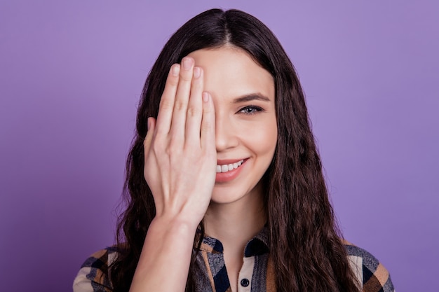 Close-upportret van meisje dat één oog gelukkige glimlach sluit die gezichtsvermogenvisie controleert die over violette kleurenachtergrond wordt geïsoleerd