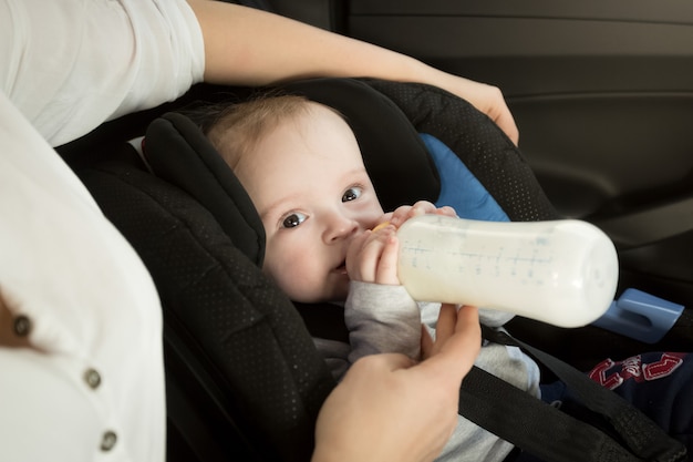 Close-upportret van moeder die baby in auto van fles voedt