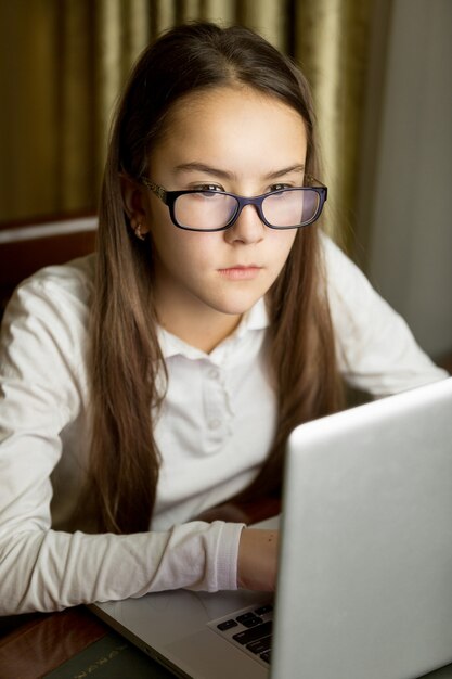 Close-upportret van mooi tienermeisje in oogglazen die laptop met behulp van