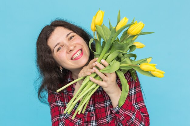 Close-upportret van mooie jonge vrouw met gele tulpen op blauwe muur.