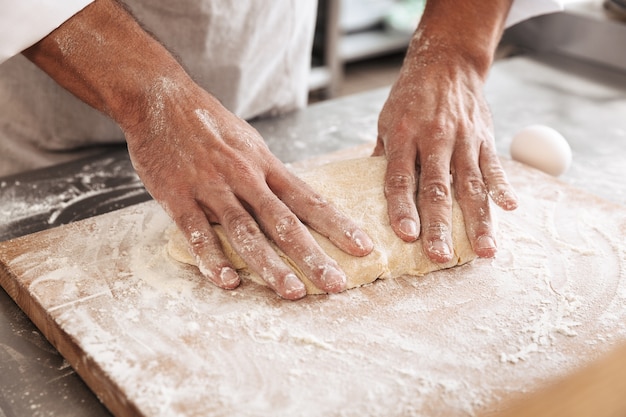 Close-upportret van mooie mannelijke handen die deeg voor brood, op lijst bij bakkerij of keuken maken