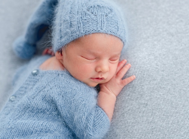 Close-upportret van pasgeboren babyjongen die gebreid lichtblauw kostuum en hoedenslaap dragen
