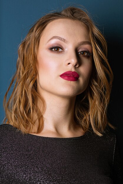 Close-upportret van prachtig blond model met lichte make-up en golvend haar, poserend in de studio