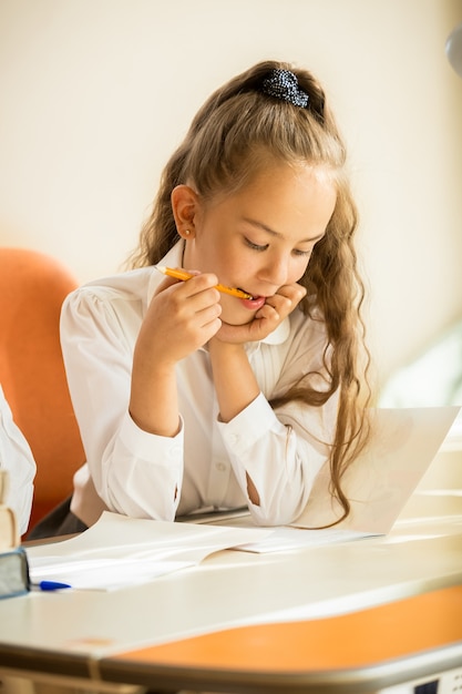 Close-upportret van schoolmeisje dat potlood kauwt terwijl ze huiswerk doet