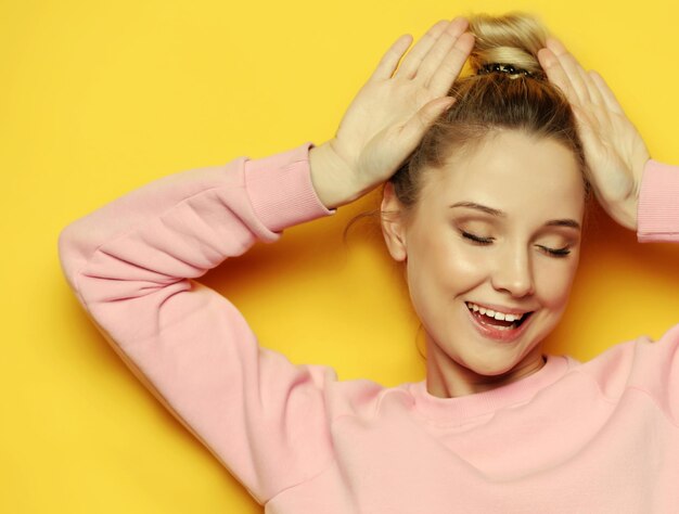 Close-upportret van speelse jonge mooie blonde vrouw die hoorns toont en gezichten maakt Geïsoleerd op gele background