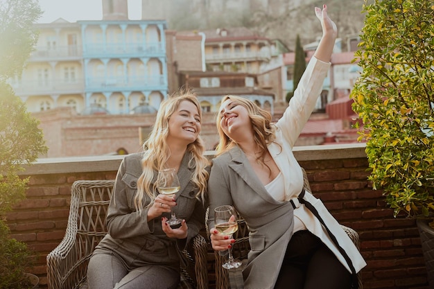 Close-upportret van twee vrouwelijke vrienden in strikte kostuums die het drinken van wijn op het terras buiten lachen