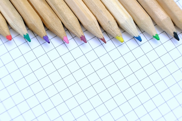 Close-upreeks veelkleurige potloden op het geruite document blad van notitieboekje voor de tekening. Terug naar school-concept.