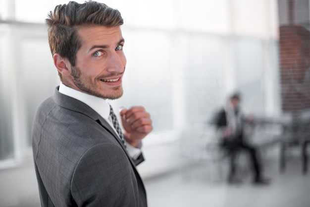 Photo close upsmiling businessman standing in front of the office window