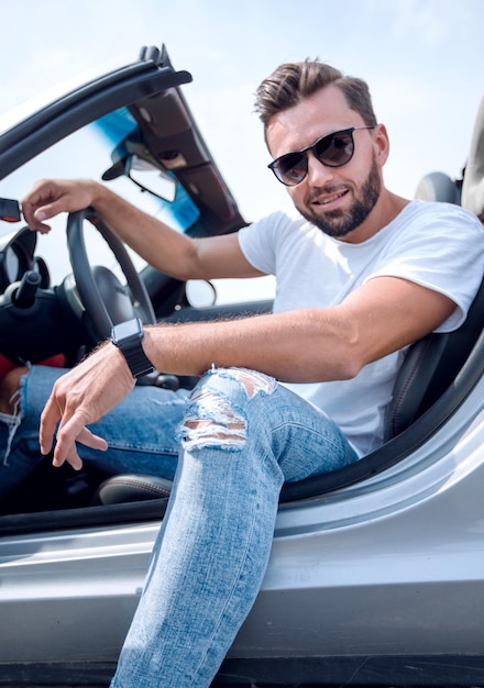 Близкий стильный молодой человек, сидящий в роскошном автомобиле, вид сбоку