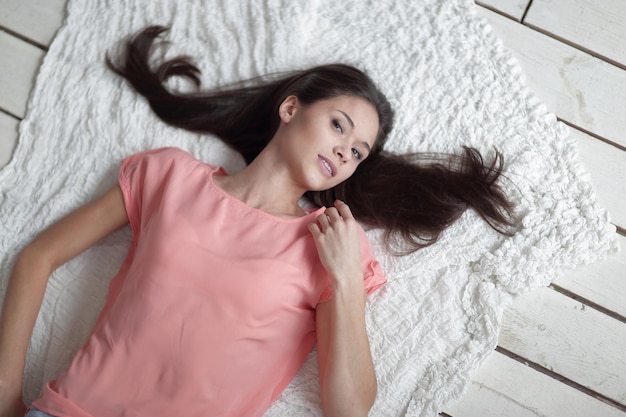 Close upthoughtful young woman lying on white carpet in living room