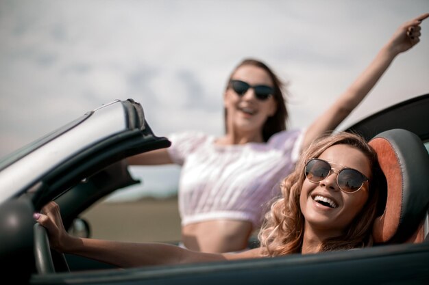 Close uptwo happy young women in a convertible car fashionable lifestyle