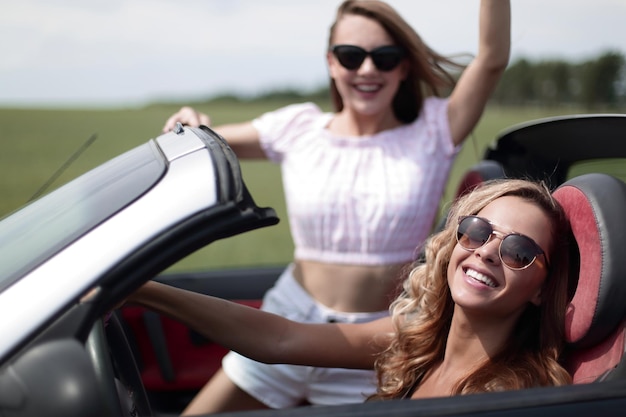 Close uptwo happy young women in a convertible car fashionable lifestyle