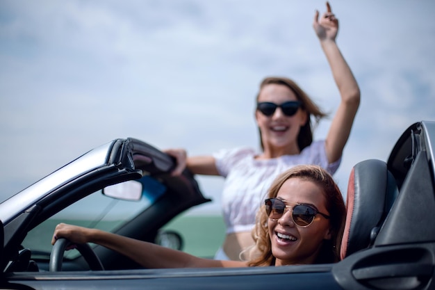 Close uptwo happy young women in a convertible car fashionable lifestyle