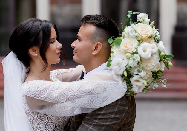 Close view of adorable brunette girl with long veil on hair and minimalistic accessories on ears dressed in wedding gown