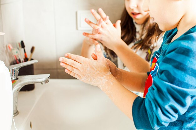 Close view of boy and girl aged 6 and 8 years washing their hands with soap and water to avoid the epidemic of the coronavirus Kids learning how to wash hands properly