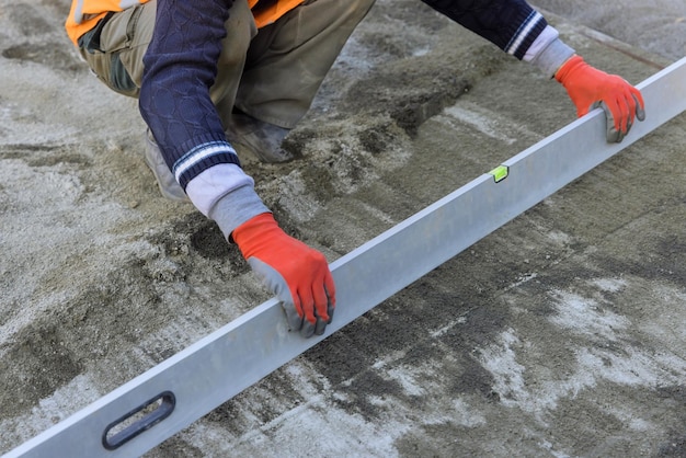 Close view of a working man holding a level tool in leveling preparation on a sandy base the paving stones