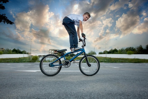 Close view of young sportive biker boy doing reckless tricks on his bike, looking into the camera. Cloudy sky background