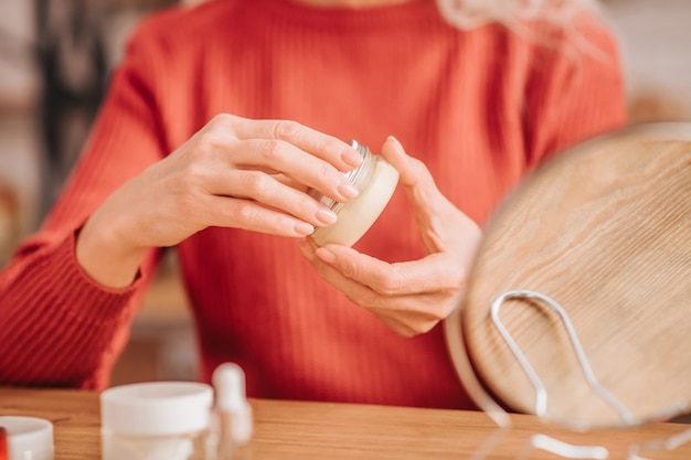 Foto in prossimità di una donna in rosso con in mano un vasetto di crema