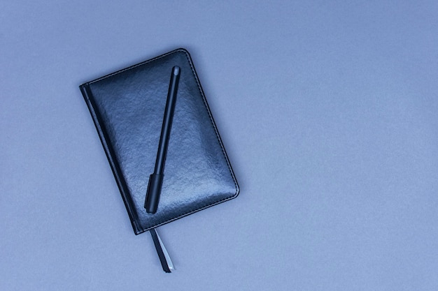 На столе лежит закрытая черная кожаная записная книжка с ручкой для заметок.