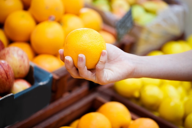 A closed hand chooses oranges on the shelf in a vegetable store