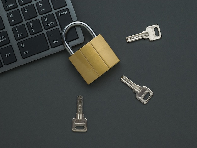 A closed lock on the keyboard and three keys on a dark table. The concept of computer security. Flat lay.