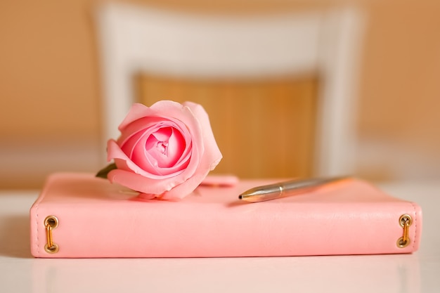 Closed notepad with pen and pink roses on white table